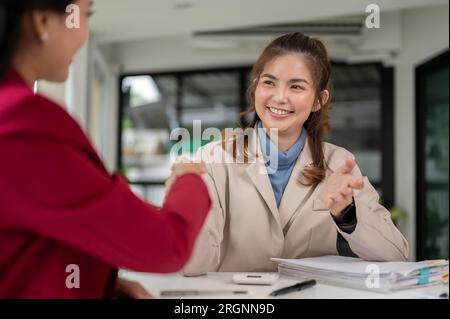 A professional and satisfied Asian female financial analyst or consultant is shaking hands with her client after the financial investment meeting. Stock Photo