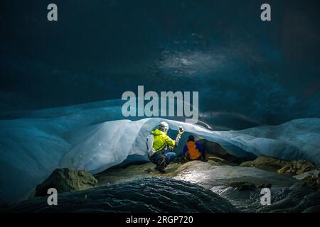 Rear view of two explorers in a low and narrow ice cave Stock Photo