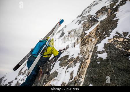 Low angle view of skier climbing up rock face towards mountain summit Stock Photo