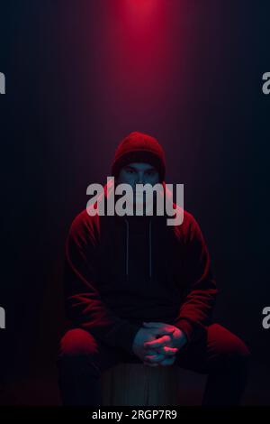 A man sitting on a stool is lit with a red light from above Stock Photo