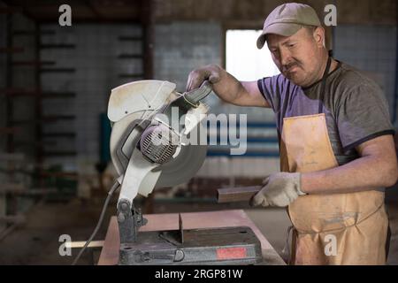 Man works in Russia. Steel cutter. Big pill in garage. Stock Photo