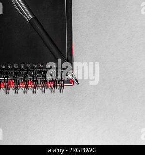 Paper notepad with spiral binder and black plastic pen lies on top. Top view. Stock Photo