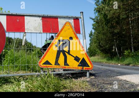 Road work ahead warning sign, hanging on a fence of construction site of new road. Roadworks traffic sign in Poland. Stock Photo