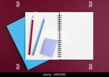 Notebook with pencil. White page on dark red color background, spiral notepad on table. Top view Copy Space. Blank paper sheet, office supplies. Greet Stock Photo