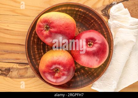 Three organic juicy apples with clay plate on wooden table, macro, top view. Stock Photo