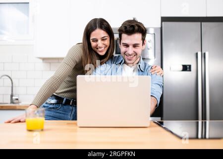 young couple planning vacations together at home looking a laptop. two cheerful young adults sitting on the kitchen. finance concept Stock Photo