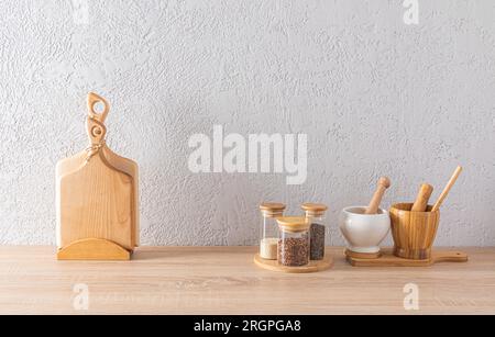 A set of glass spice jars, two mortars with a pestle, cutting wooden boards on the kitchen countertop. minimalism in the interior of a modern kitchen Stock Photo