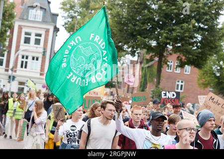 11 August 2023, Lower Saxony, Lüneburg: A participant of a protest march of the climate movement Fridays for Future carries a flag with the inscription 'Fridays for Future Ukaine'. The demonstration through Lüneburg is intended, among other things, to draw attention to the need for the new Hamburg-Hanover rail line. Photo: Georg Wendt/dpa Stock Photo