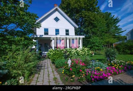 Beautiful white historic house built in 1856 with two flags hanging from the porch and a flower garden out front with a statue of St. Francis Assisi. Stock Photo