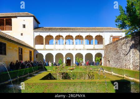 Alhambra, Spain, group of tourists visiting an interior backyard garden with fountain. A two stories medieval building is in the distance. Alhambra is Stock Photo