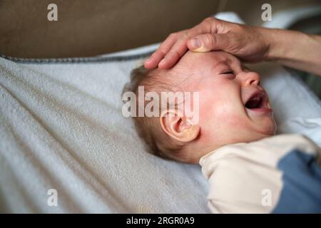 Parent trying to calm an agitated baby crying in pain Stock Photo