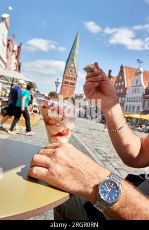 11 August 2023, Lower Saxony, Lüneburg: A man enjoys a large ice cream sundae in a cafe on the square Am Sande on this sunny and warm summer day. Photo: Georg Wendt/dpa Stock Photo