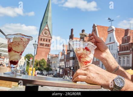 11 August 2023, Lower Saxony, Lüneburg: A man enjoys a large ice cream sundae in a cafe on the square Am Sande on this sunny and warm summer day. Photo: Georg Wendt/dpa Stock Photo