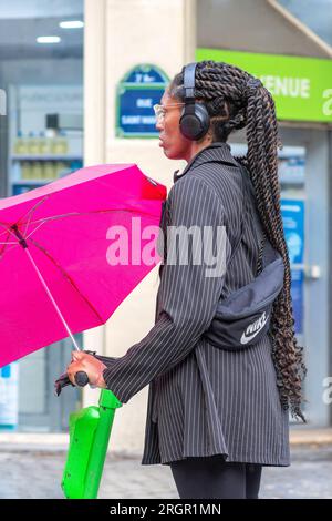 Young black woman with plaited hairpiece and umbrella in rainy Paris, France. Stock Photo