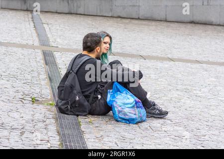 Young couple sat on cobbled square talking together - Paris, France. Stock Photo