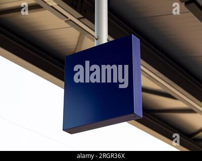 Empty blue sign hanging from the rooftop in a public area. The squared metal plate is blank and can be used as a template. Stock Photo