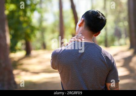 Back view of Asian man rubbing neck painful cramp during trail running in forest Stock Photo