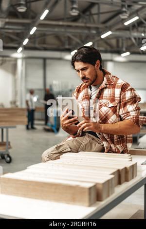 Young carpenter standing in his workshop using a digital tablet Stock Photo