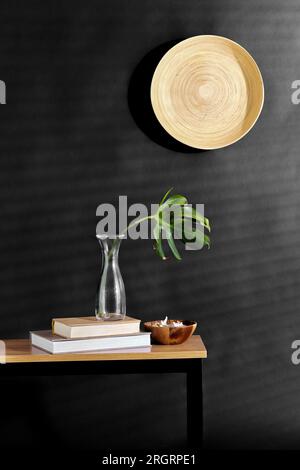 monstera leaf in vase, books and shells on bench Stock Photo
