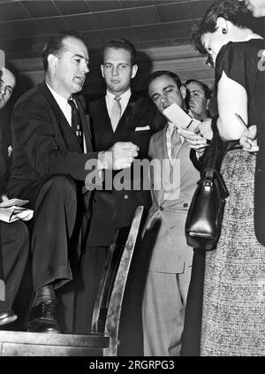 New York, New York:  1953    Senator Joseph R. McCarthy (left), discusses the State Department's Voice of America program with newsreporters in New York, while associates David Schine (center) and Roy Cohn (right) stand by. Stock Photo