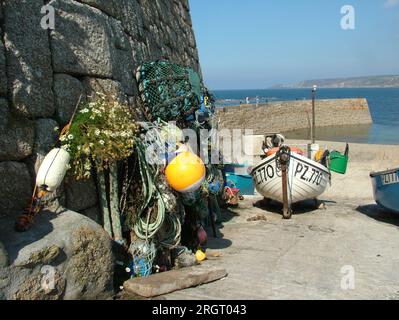 Fishing nets, lobster pots and marker bouys waiting to be loaded onto the small fishing boats lined up on the slipway in Sennan cove with the breakwat Stock Photo