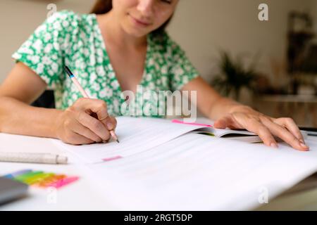 Adult university student woman sitting at the desk at home and doing homework, doing the exercise in the workbook, pencil in female hand. Stock Photo