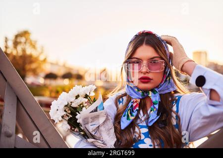 Charm of a woman adorned in an exquisite blue traditional dress, carrying a blue handbag and a bouquet of flowers, gracefully strolling through the Stock Photo