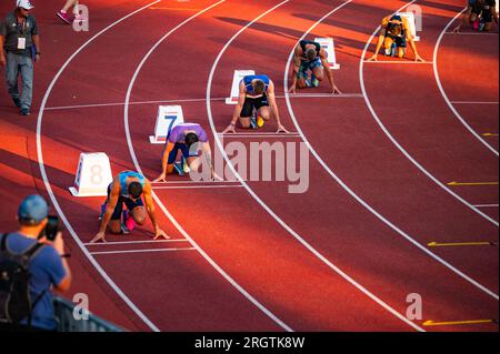 B. BYSTRICA, SLOVAKIA, JULY 20, 2023: Male Sprinters Poised at the Beginning of 200m Race Under Serene Sunset Light Stock Photo