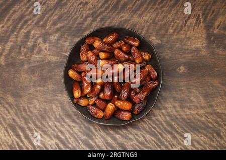 Dates in a plate on a wooden background. Dried fruit on a brown table. Copy space, top view, flat lay. Stock Photo
