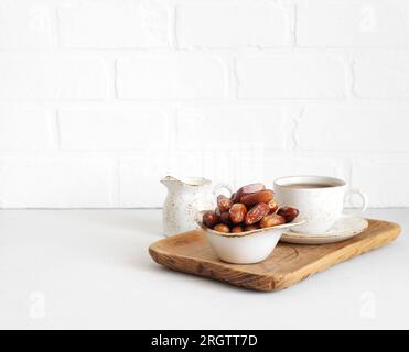 Dried dates in a bowl, tea in a wooden tray on a white background. Healthy breakfast. Natural oriental sweets. Copy space. Stock Photo