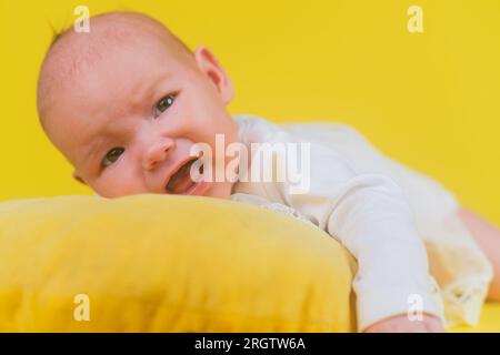 Cute newborn baby girl screams and crying on a yellow pillow, closeup Stock Photo