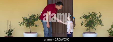 Image of a young dad holding his daughter's hand as he walks her out of the house. Father and daughter holding hands Stock Photo