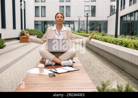 Woman freelancer working on laptop while sitting outside in lotus position on office background Stock Photo
