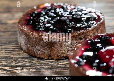 dessert of baked tartlets, chocolate tartlet with fruit and berry filling, round tartlet with strawberries and blueberries in butter cream, closeup Stock Photo
