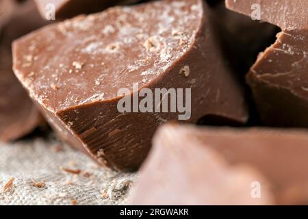 pieces of bitter chocolate are randomly scattered on the table, broken and crumbled natural bitter chocolate, edible bitter chocolate made from cocoa Stock Photo