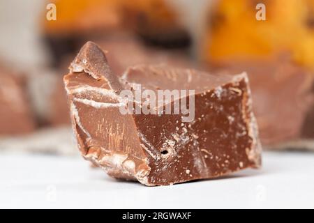 edible milk chocolate made from cocoa and sugar, pieces of chocolate randomly scattered on the table, broken and crumbled natural chocolate Stock Photo
