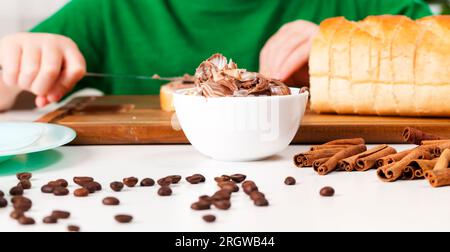 a child prepares sweets in the kitchen from a roll and chocolate, chocolate butter that the child puts on a loaf of bread cut into pieces, a child wit Stock Photo