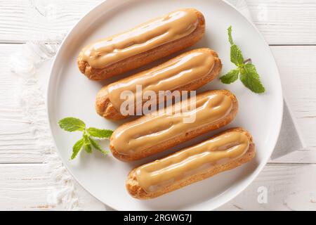 Eclairs with custard and caramels icing topped close-up in a plate on the table. Horizontal top view from above Stock Photo