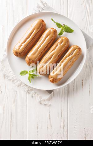 Fresh classic eclairs with cream filling and covered with caramel sauce close-up in a plate on the table. Vertical top view from above Stock Photo