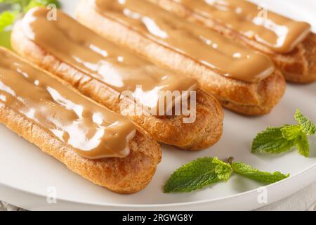 Eclairs with custard and caramels icing topped close-up in a plate on the table. Horizontal Stock Photo