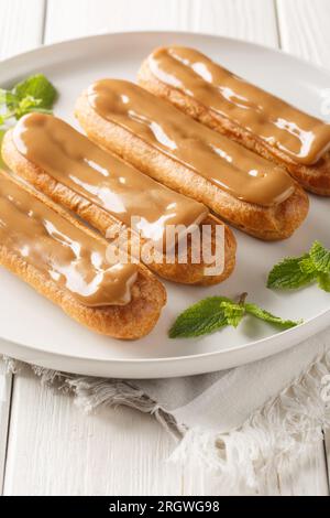 Traditional french eclairs filled with coffee cream close-up in a plate on the table. Vertical Stock Photo