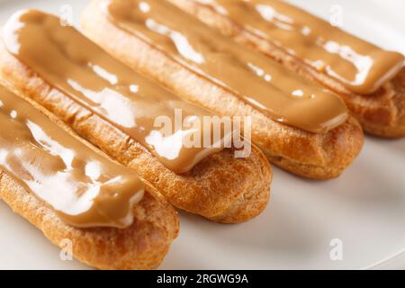 Fresh classic eclairs with cream filling and covered with caramel sauce close-up in a plate on the table. Horizontal Stock Photo