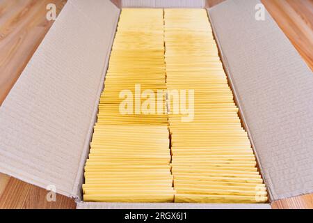 Close-up of an open shipping box filled with yellow padded envelopes placed on a wooden floor. Stock Photo