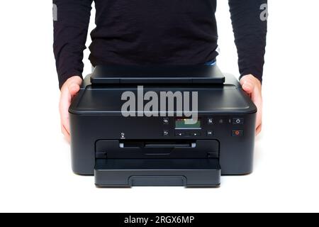 Person wearing a black longsleeve holds a modern inkjet printer with both hands on a clean white backdrop. User-friendly technology and portability re Stock Photo