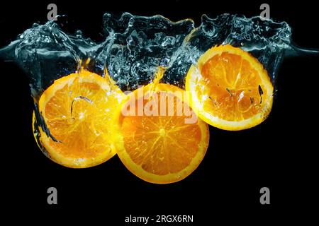 Close-up of three sliced oranges plunged underwater with splashes on black. Stock Photo
