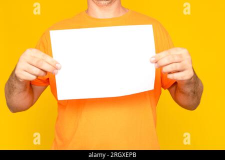Half-length image of a man holding a blank sheet of paper making an advertising billboard, isolated over yellow background. Stock Photo