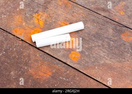 Two white school chalks placed on obsolete brown and rusty wooden planks of table. Stock Photo