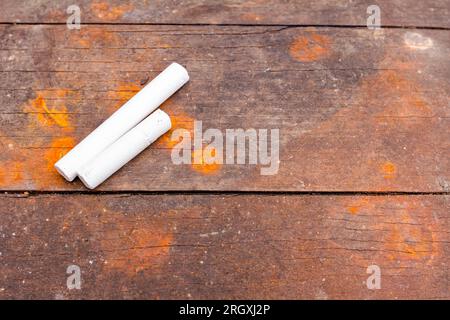 Two white school chalks placed on obsolete brown and rusty wooden planks of table. Stock Photo