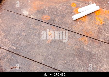 Two white school chalks placed on obsolete brown and rusty wooden planks of table. Stock Photo