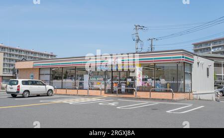 A storefront or exterior of a busy 7-Eleven, a famous Japanese convenience store located on a busy intersection on a sunny summer's day. Stock Photo